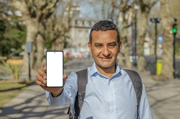 Latin man in a city shows the screen of his mobile phone