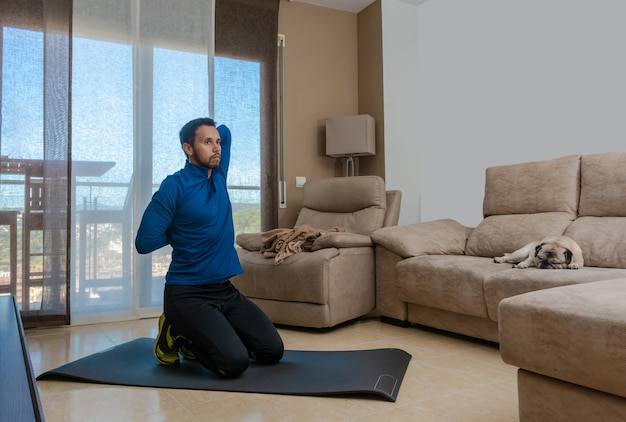 Latin man, doing a workout in his living room, does sit-ups, stretches and squats