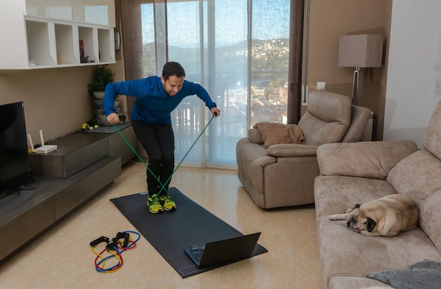 Latin man, doing a workout in his living room with a rubber band while taking an online class