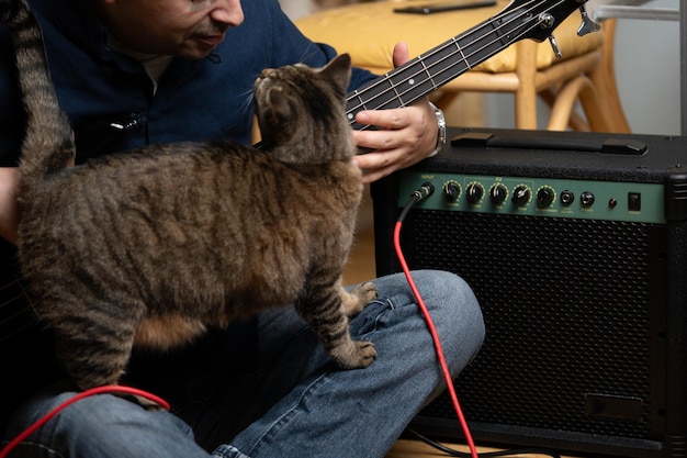 Латинский мужчина учится играть на электрическом басу, общаясь со своей кошкой.