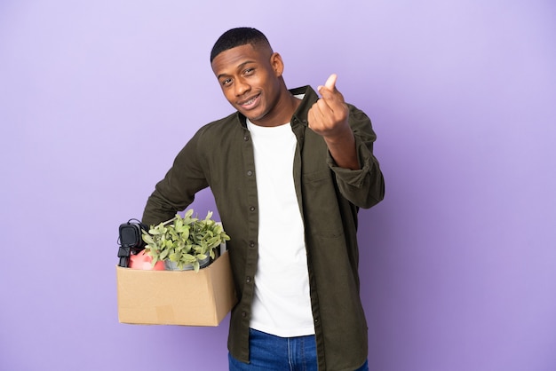 Latin man making a move while picking up a box full of things making money gesture