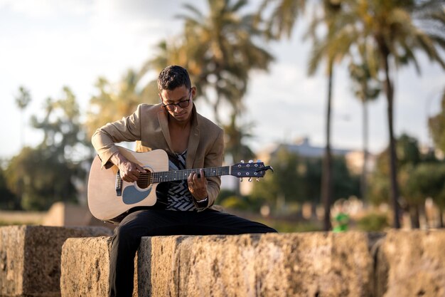 Photo latin man playing guitar on the street during sunset in panoramic