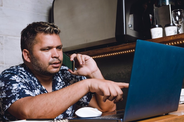 latin man in a restaurant talking on the phone and pointing at the computer with his finger