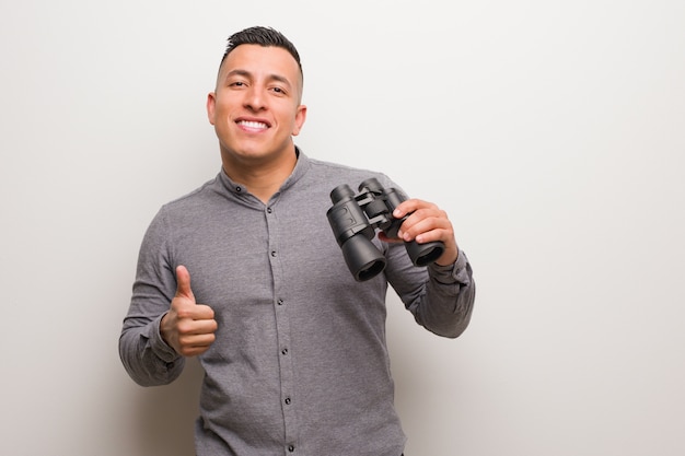 Latin man smiling and raising thumb up. He is holding a binoculars.