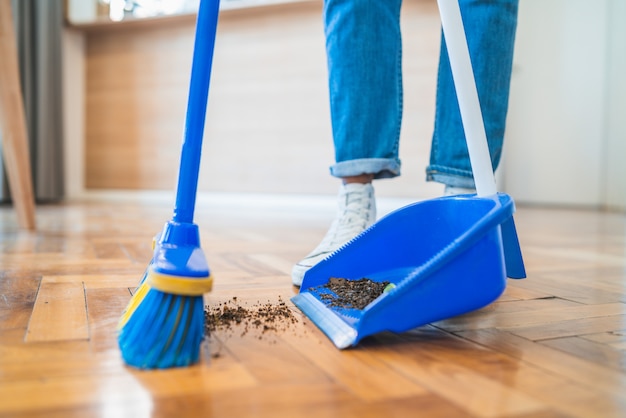 Latin man sweeping wooden floor with broom at home.