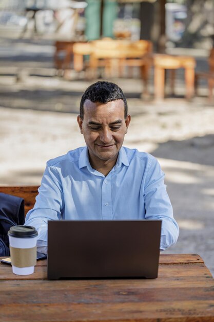 Latin man using laptop at outdoor bar table