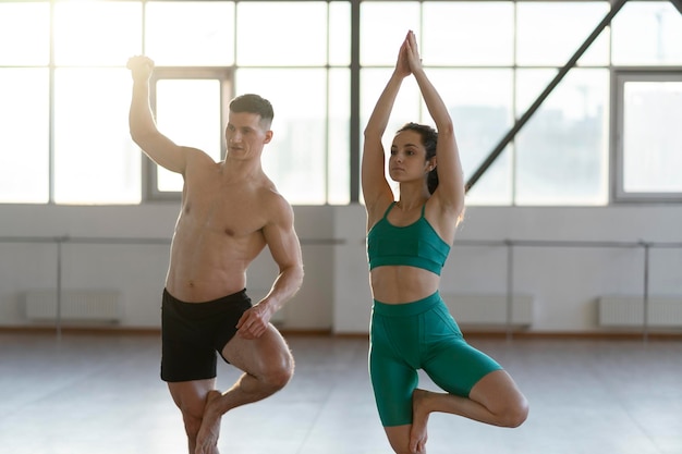 Uomo latino e donna che si allenano in palestra facendo yoga in piedi su una gamba concetto di vita sana