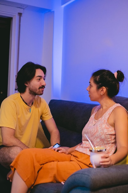 Latin man and woman young friends talking sitting on the sofa gossiping drinking mate