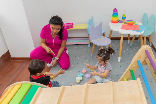 의사 사무실의 놀이방 바닥에 있는 두 아이와 노는 라틴 간호사