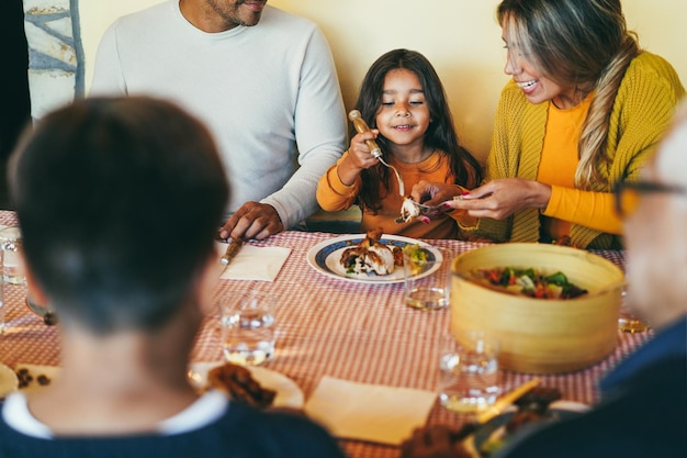 Foto genitori latini che si divertono con i bambini durante la cena a casa focus sul viso della ragazza