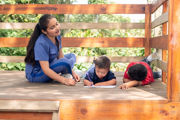 라틴계 소아과 의사가 두 어린이를 위한 작업 치료 세션에서 일하고 있습니다. 그림을 그리는 아이들.