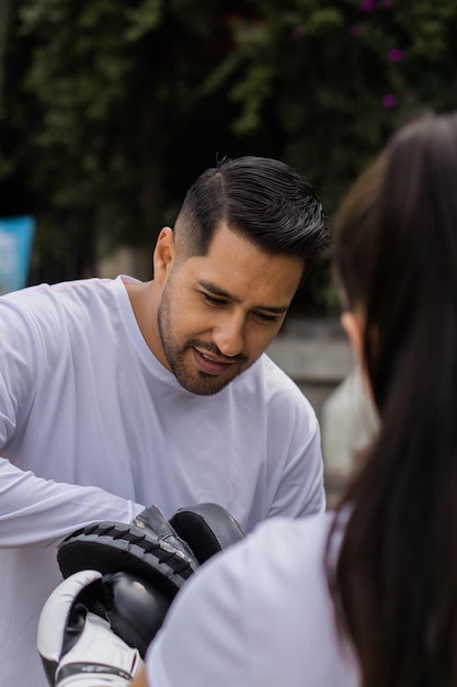 Latin trainer using boxing mitts and gloves with his apprentice in a park.