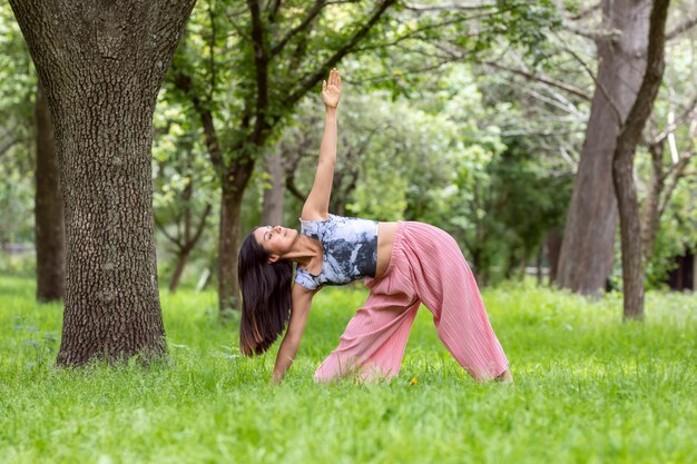 草や木々のある屋外公園でさまざまな姿勢でyogaasanasをやっているラテン女性...