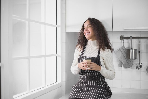 キッチンで朝食をとりながらコーヒーを飲むラテン系女性。