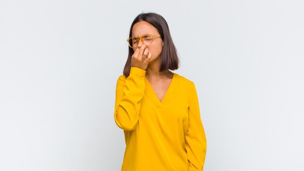 Latin woman feeling disgusted, holding nose to avoid smelling a foul and unpleasant stench