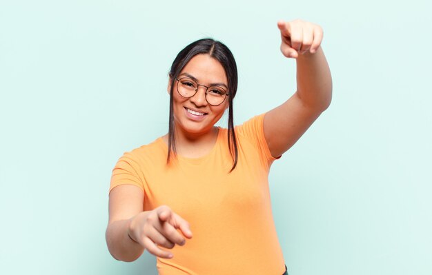 Latin woman feeling happy and confident, pointing to camera with both hands and laughing, choosing you