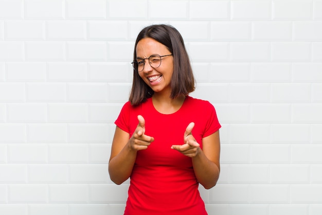 Latin woman feeling happy, cool, satisfied, relaxed and successful, pointing at camera, choosing you