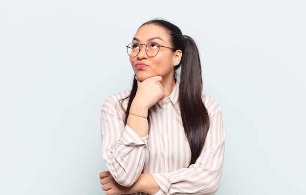 Latin woman feeling thoughtful, wondering or imagining ideas, daydreaming and looking up to copy space