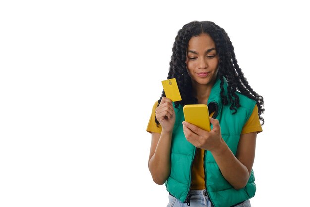 Photo latin woman holding a mobile phone and a credit card while standing over an isolated background.