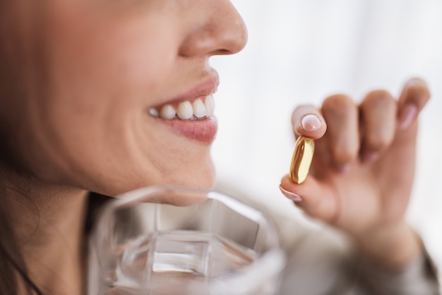 Latin woman holding a Omega 3 fish oil capsule at home.