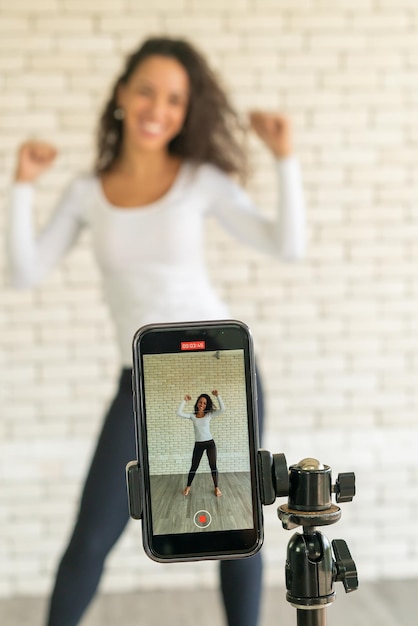 Latin woman influencer created her dancing video by smartphone camera. To share video to social media application.