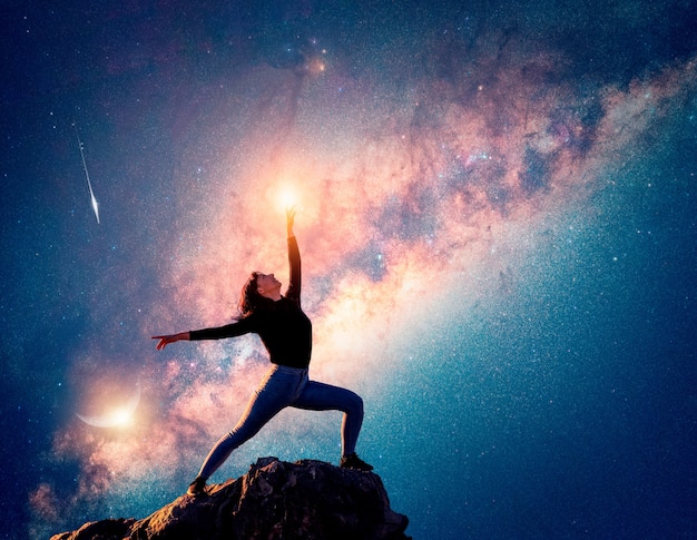 латинская женщина танцует или позирует на вершине горы, указывая на небо и Млечный Путь