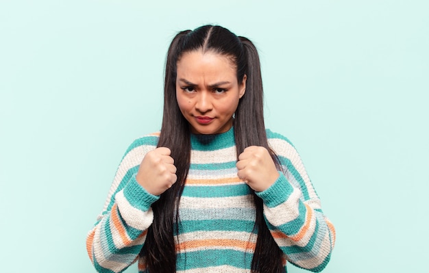 Latin woman looking confident, angry, strong and aggressive, with fists ready to fight in boxing position