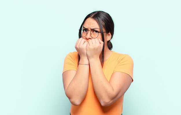 Latin woman looking worried, anxious, stressed and afraid, biting fingernails and looking to lateral copy space