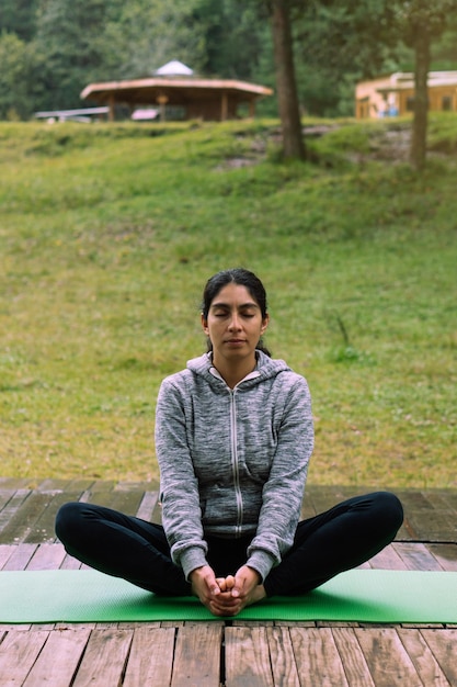 Latin woman in lotus position practicing yoga in a forest.