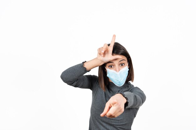 A latin woman mocking to the camera and making the L or looser sign while wearing a face mask