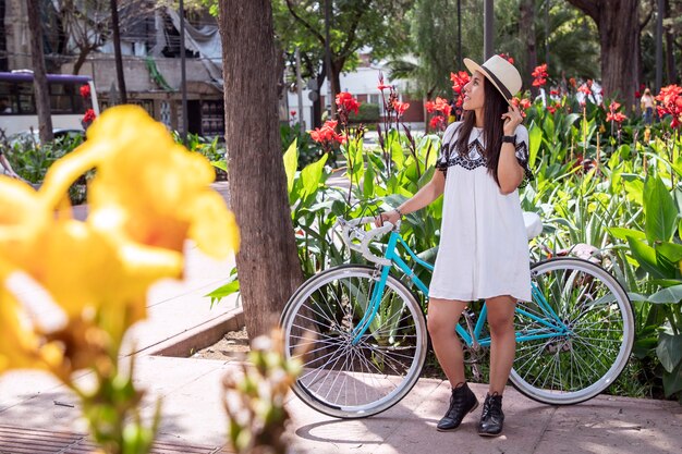 Foto donna latina in un parco con la sua bicicletta che indossa vestito e cappello