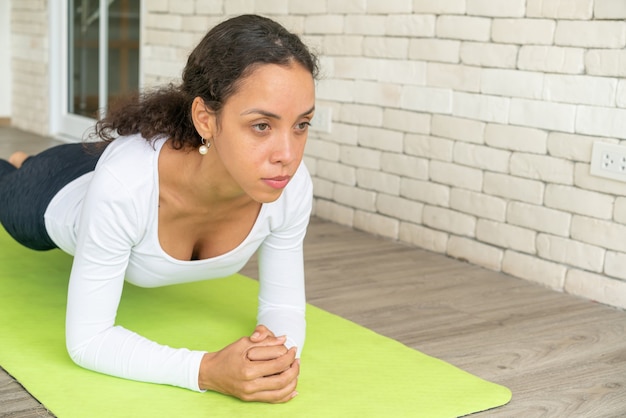 Latin woman practicing yoga on mat with white brick background