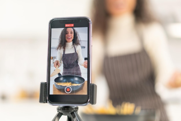 Latin woman shooting video and cooking at the kitchen for share on blog