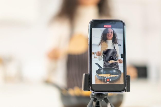 Photo latin woman shooting video and cooking at the kitchen