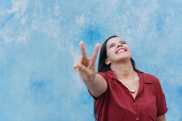 Latin woman showing peace sign while standing by wall