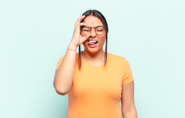 Latin woman smiling happily with funny face, joking and looking through peephole, spying on secrets