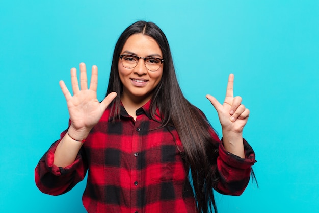 latin woman smiling and looking friendly, showing number seven or seventh with hand forward, counting down