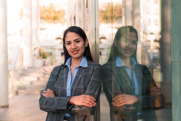 Latin woman smiling with her arms crossed leaning against an office building