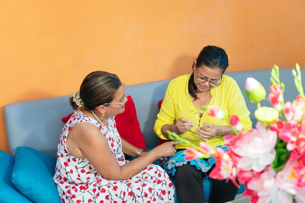 Latin woman teaching her friend the art of knitting woolen clothes