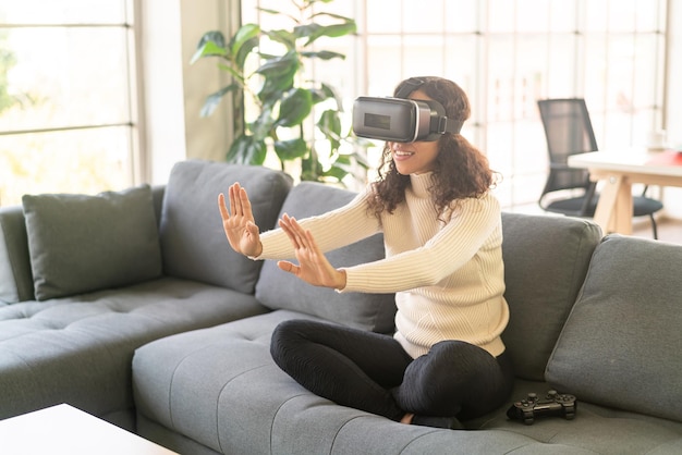 Donna latina che utilizza un auricolare per realtà virtuale sul divano di casa