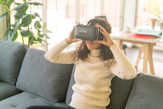 Latin woman using a virtual reality headset on sofa at home