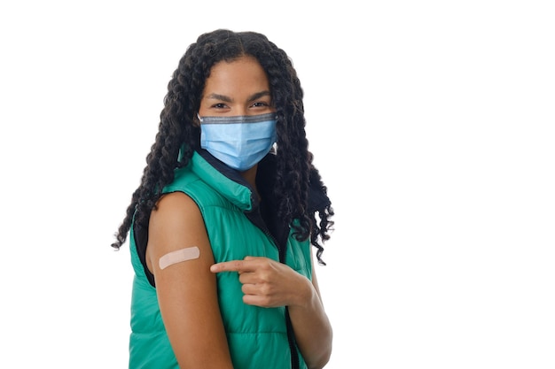 Covid-19に対するワクチンを接種した後、バンドエイドで腕を見せながらフェイスマスクを着用しているラテン系女性。医学と予防接種の概念。