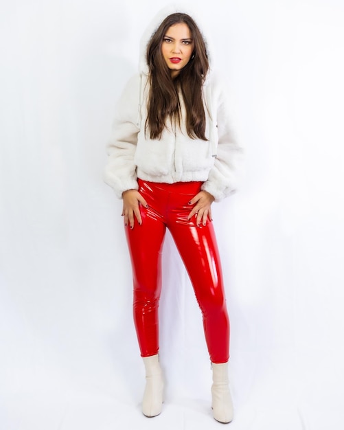 Latin woman with black hair wearing a white wool sweater and red latex pants photographed in a studio with a white background
