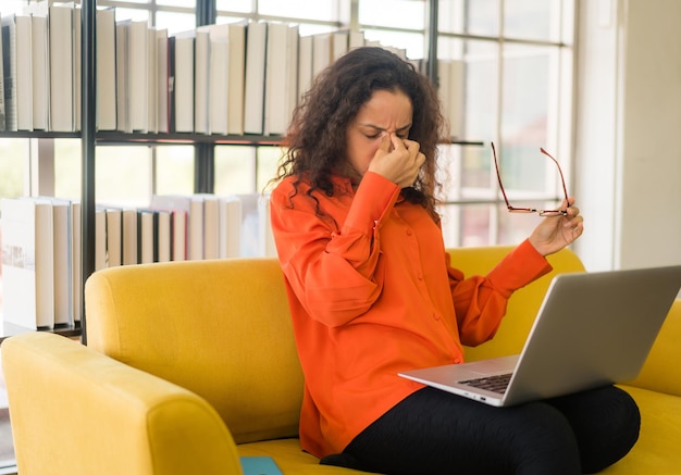 Latin woman working with laptop on sofa with tired feeling