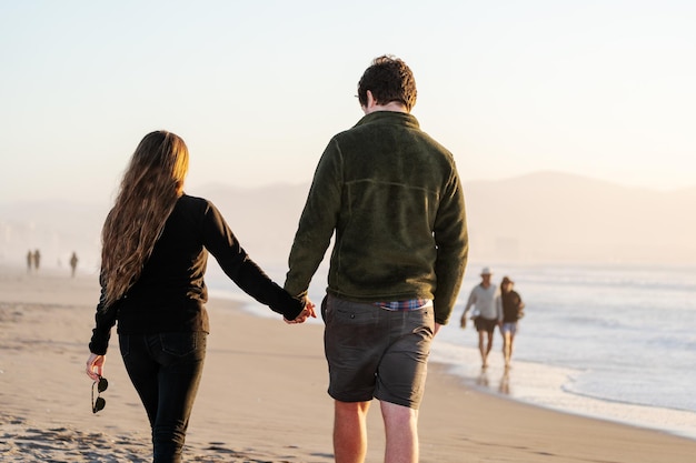 Latin young couple in love walking on the beach holding hands in La Serena Chile back view
