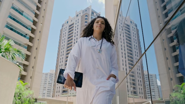 Latin young female doctor wear white uniform, using digital tablet in hospital