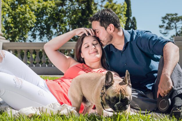 公園の芝生の上に横たわっている彼のガール フレンドに頭のキスを与えるラテンの若い男