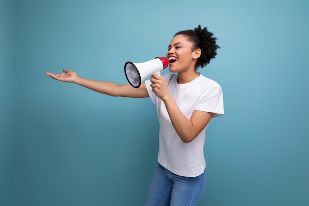 Latin young woman dressed in a white tshirt and talking a message into a megaphone on a blue