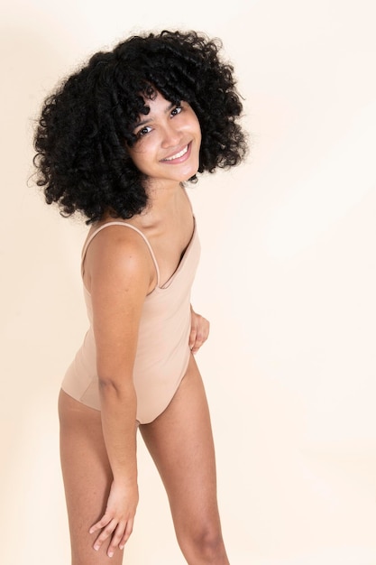 Latina girl with afro hair dressed in a bodysuit smiling and showing her body proud of her body