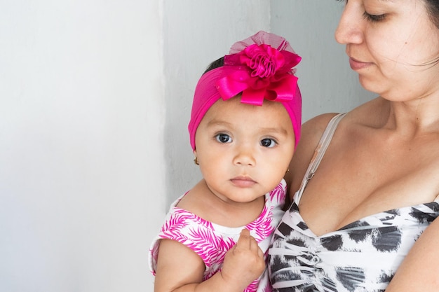 Latina mother holding her brunette baby in her arms looking at her with pride girl with curious look